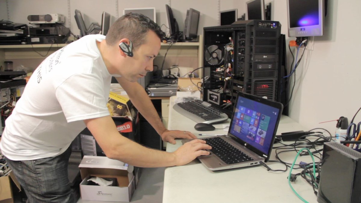 Technician working on a computer with a gaming system nearby